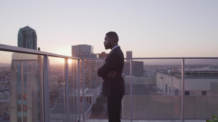 A man stands on a high roof top balcony in the city