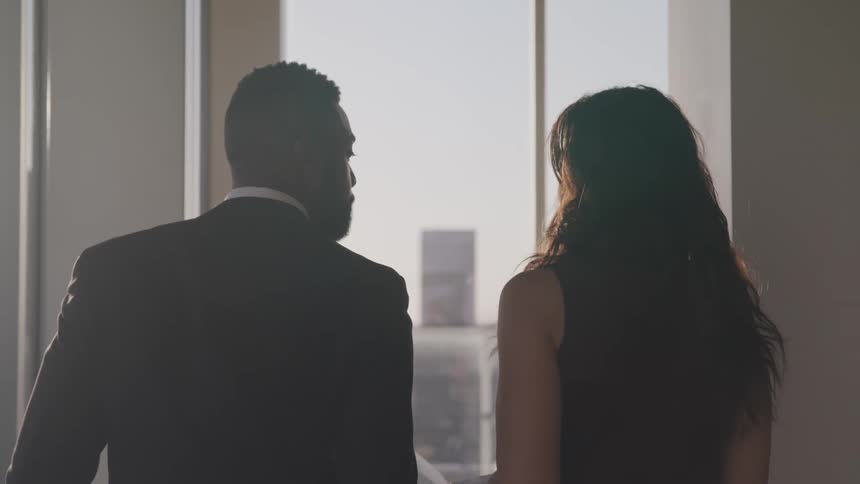 Two business people talking in the office walk towards a window at sunset