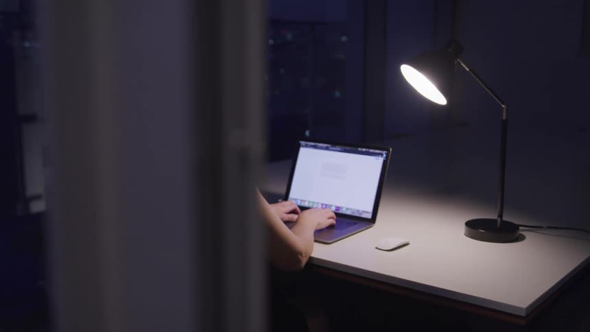 A woman is typing on a computer at night