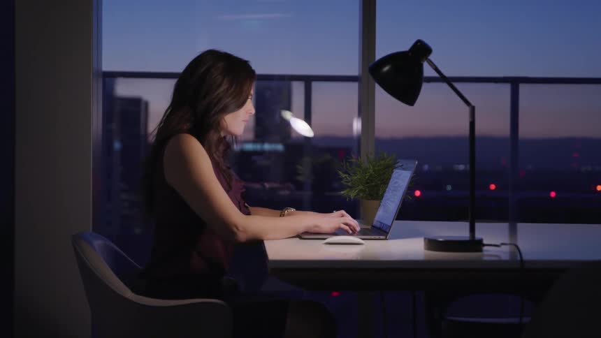 Businesswoman sitting at a table uses a laptop in the office at dusk