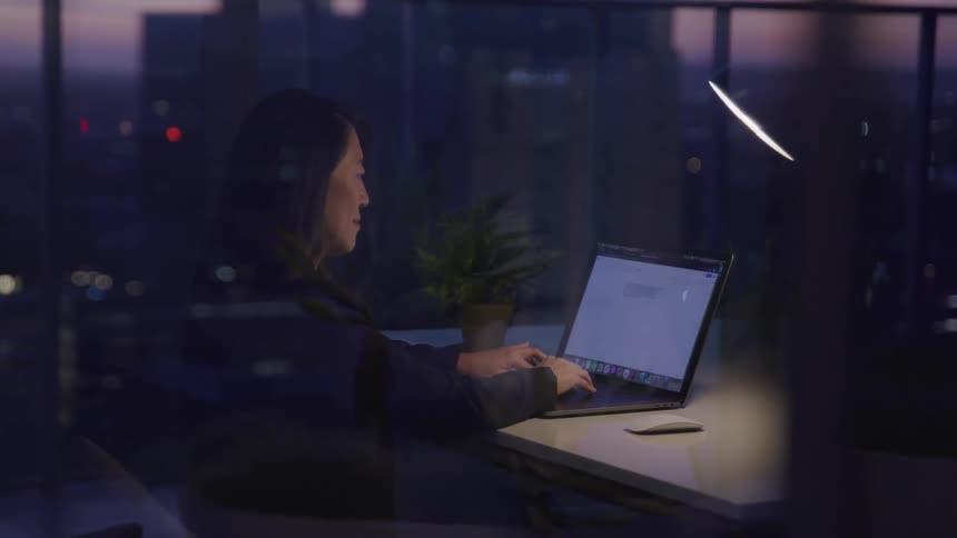 Asian businesswoman sits at a desk and uses a laptop in the office at dusk
