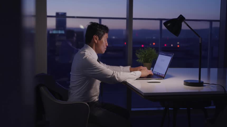 Asian businessman with a suit sitting at a table uses a laptop in the office at dusk