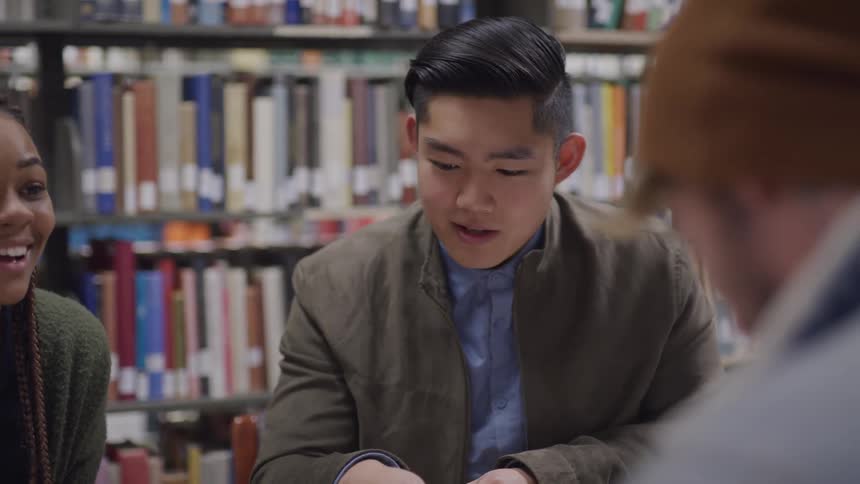 Three friends talk and laugh as they sit in the library