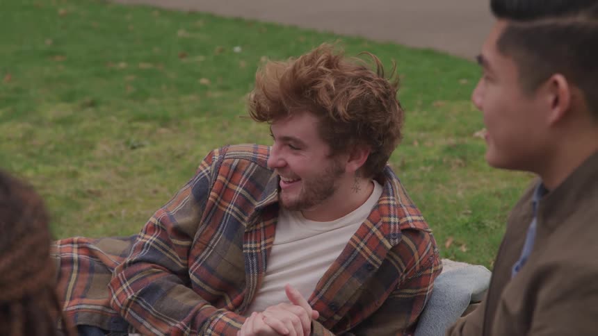 A group of friends sit outside on the grass and talk