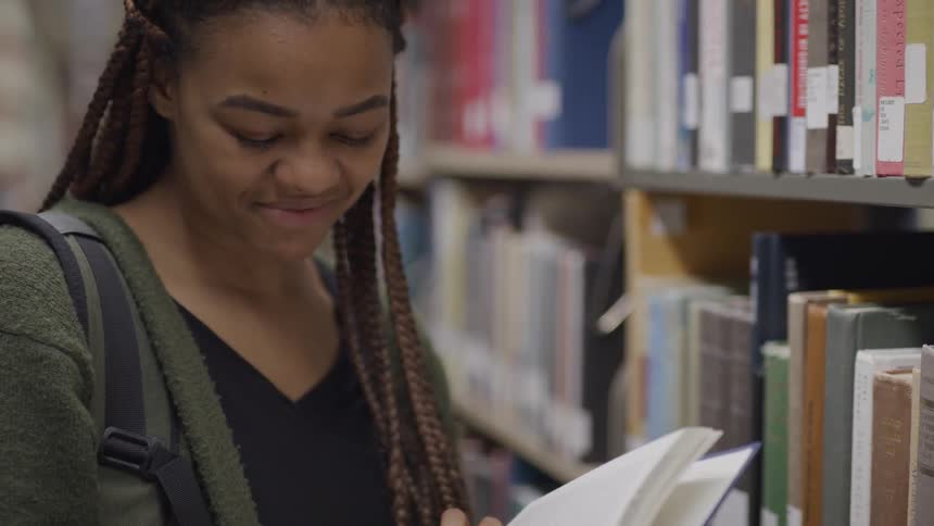 Black girl with braided hair looks through a book in the library