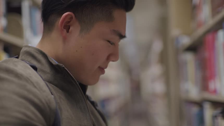 An asian male in a library reading from a book