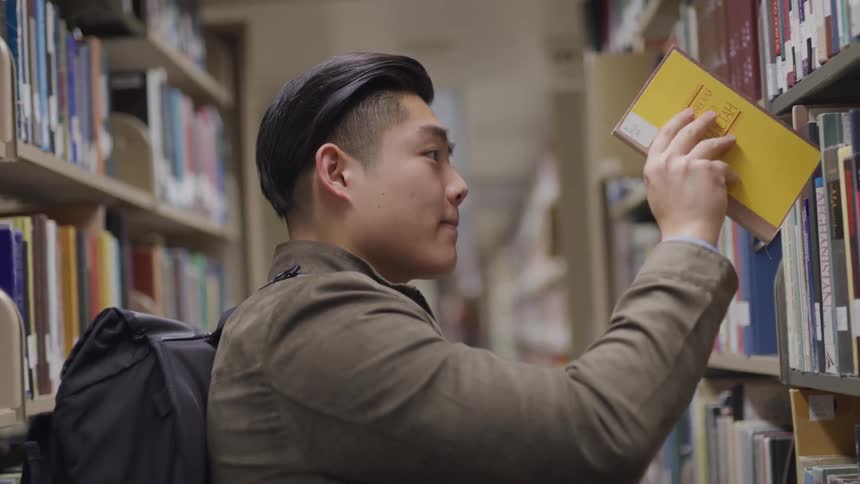A man with a backpack putting a book on a shelf in a library