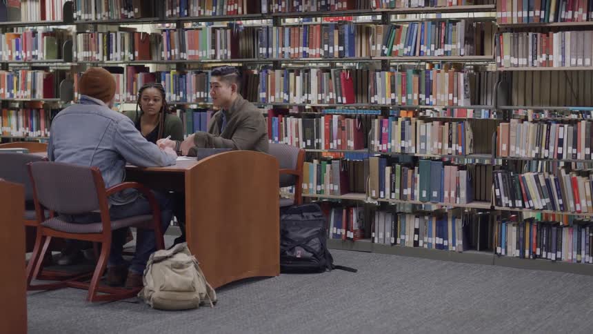 Three people sit at a desk together inside a library