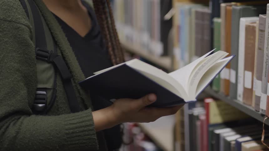 Black girl with braided hair leafs through a book in the public library