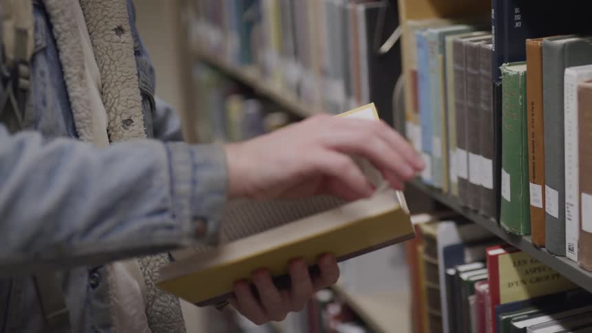 Person in a library reading a book from book shelf