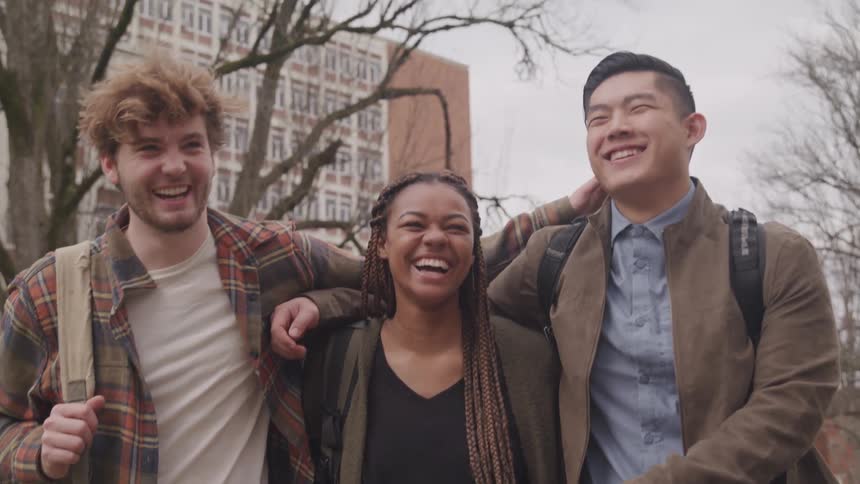 Three university classmates smile and laugh as they walk through campus on a cool fall day