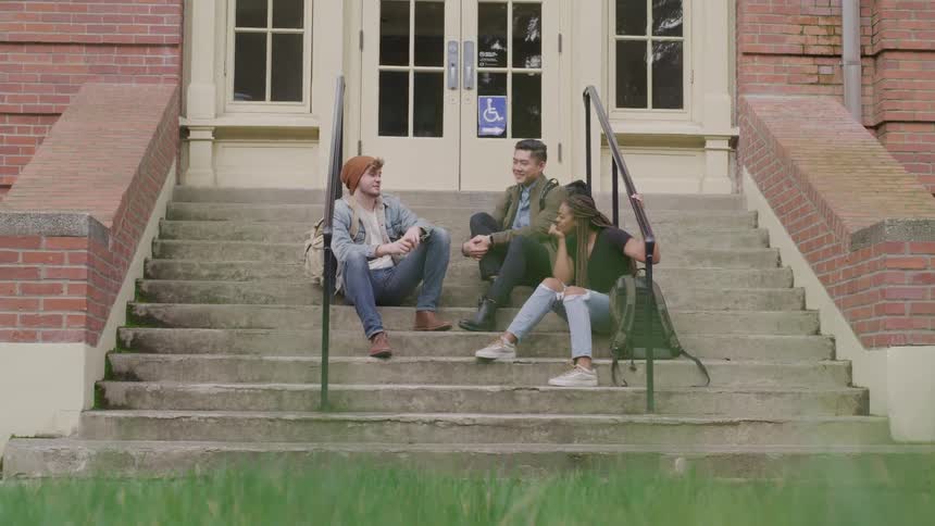 Two men and a woman sitting on a staircase in front of a building