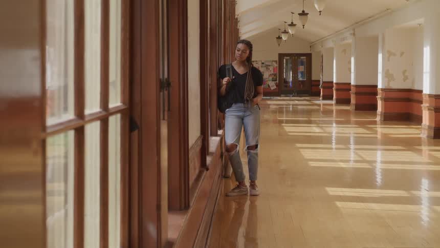 A teenager stands in a school hallway and looks out the window