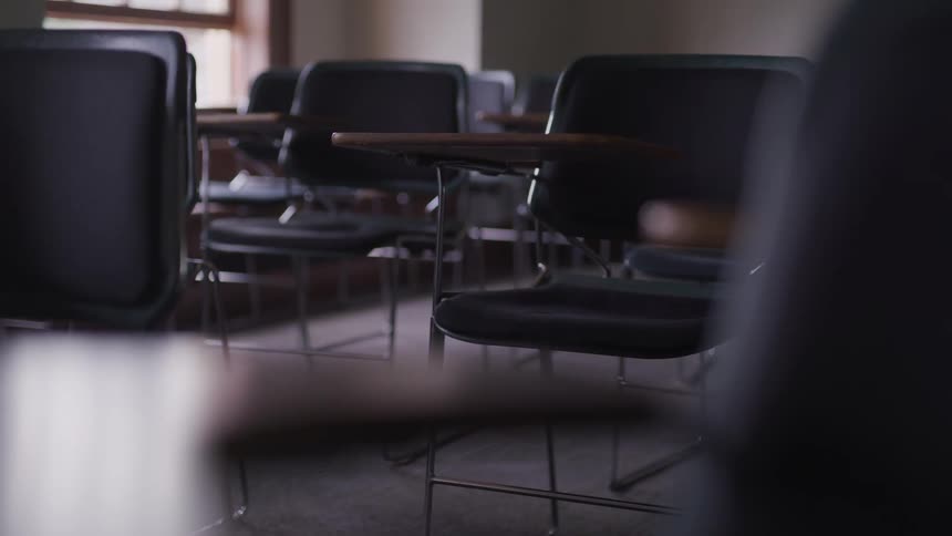 Several empty school desks are lined up inside of an unoccupied classroom