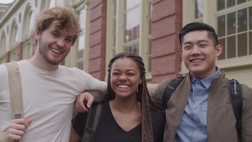 Group of friends hug each other laughing outside a building looking at the camera