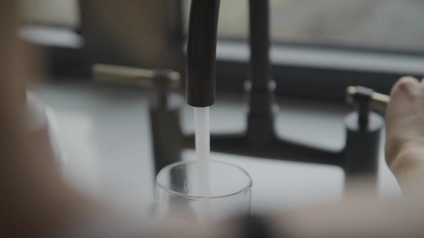 A person is filling a cup with water from the sink