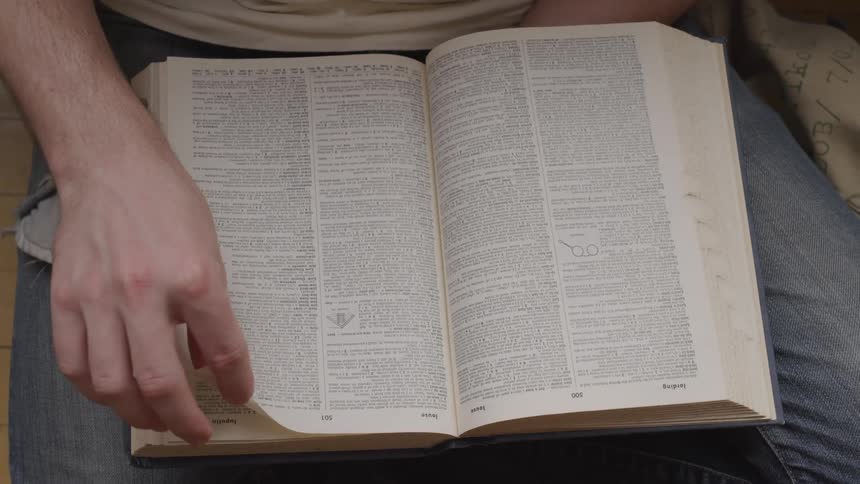Person flips through dictionary resting in their lap