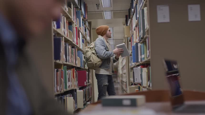 Man with a brown beanie denim jacket and ripped jeans searches for a book in the public library