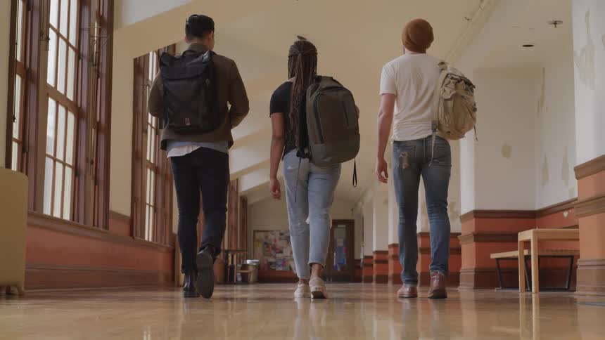 Three college students walk down a hallway with backpacks