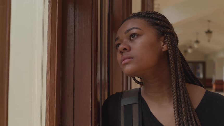 A woman gazes out of the window in a long hallway