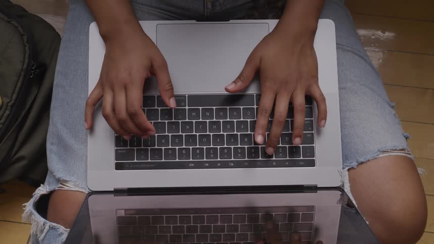 A teenage girl with a laptop on her knee types on it