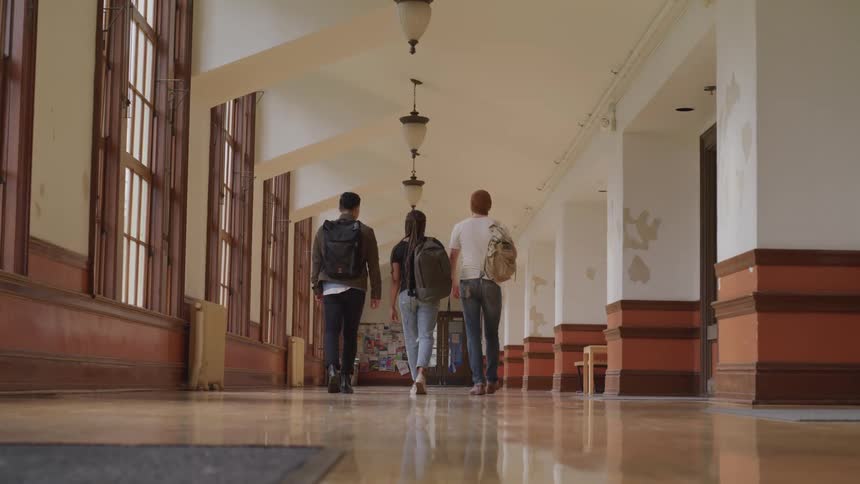 A trio of students carrying backpacks walk together down a school hallway