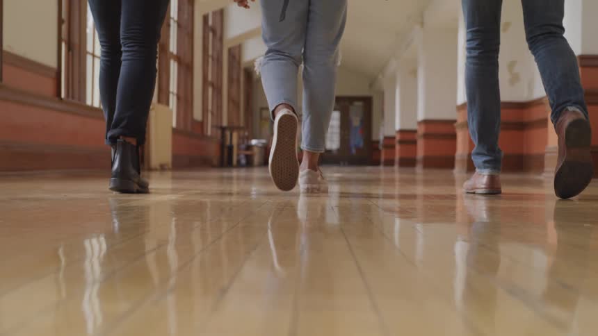 Three people walking down a hallway with only their legs showing