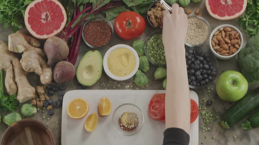 A person uses a metal school and their bare hands to transfer food from a table to a small glass bowl on a cutting board