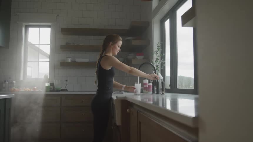 Woman filling glass with water from kitchen sink