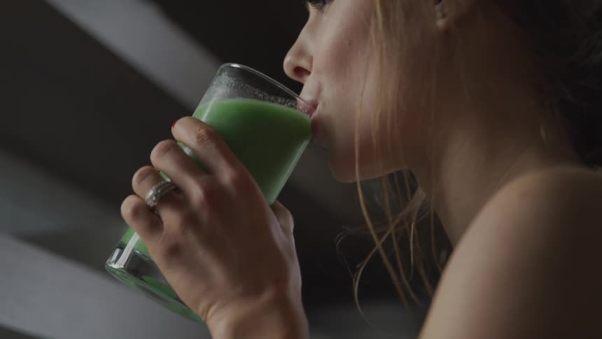 Woman with brown hair and a wristwatch drinks a smoothie made from fruit and vegetables in the kitchen