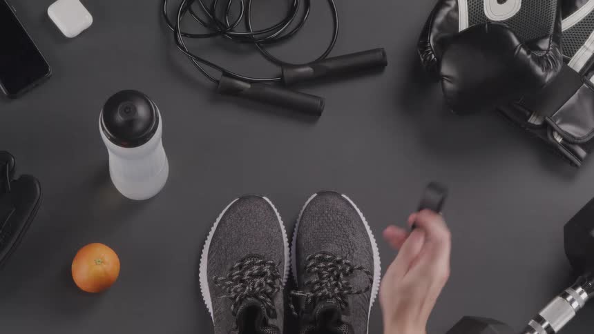 A woman picks up her smart watch and running shoes which are close to other workout gear