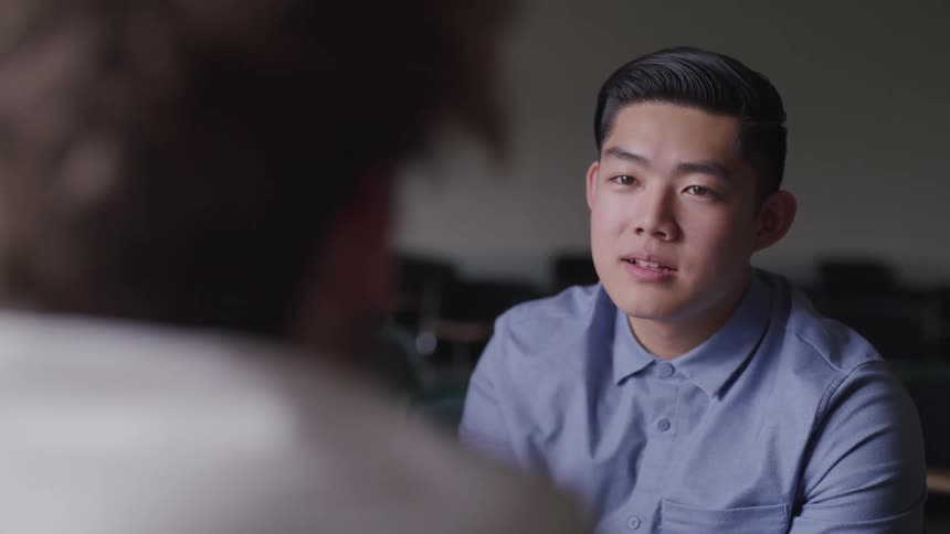 Young man listening to a teacher while sitting in a classroom