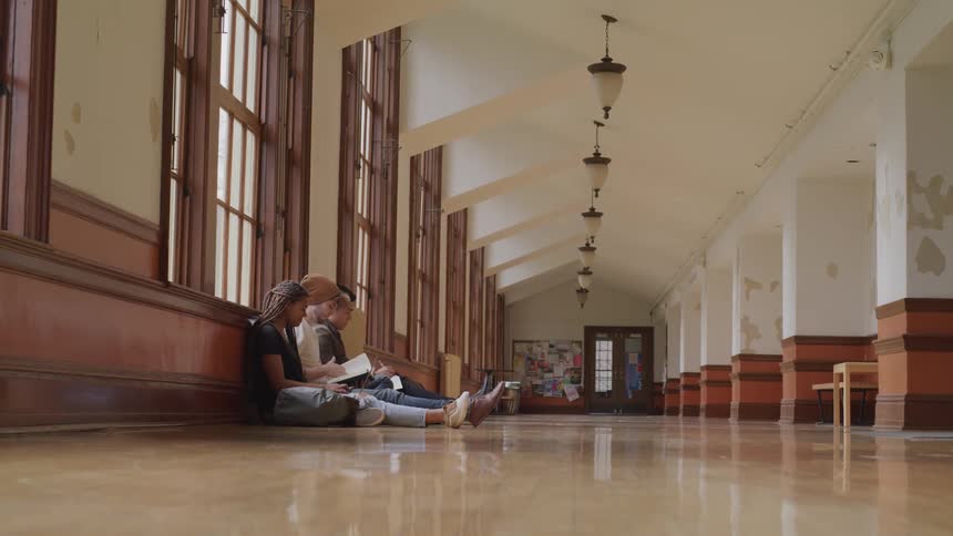 A group of students study together on the floor of a school hallway