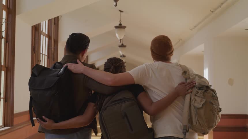 A group of students wrap their arms around one another as they walk down a school hallway