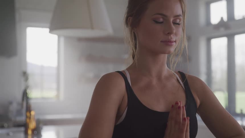A woman stands in her kitchen with her hands folded in a yoga pose