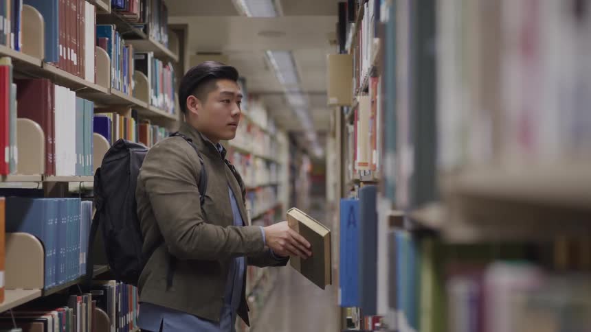 University students searches for books in the library shelfs