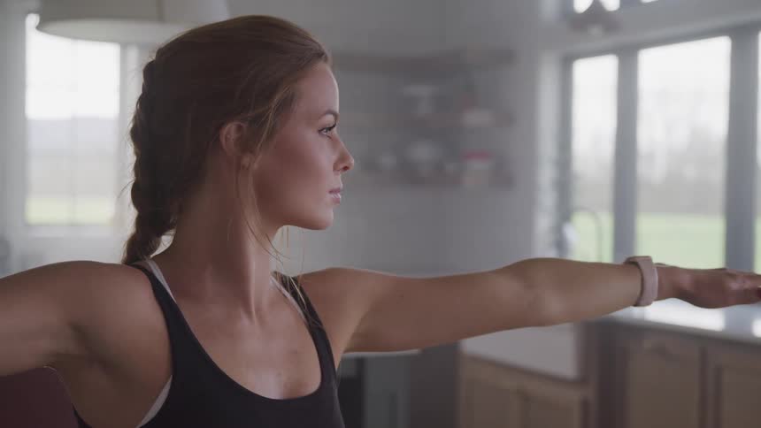 Woman with a french braid hair and a black sports bra does some stretching exercises at home
