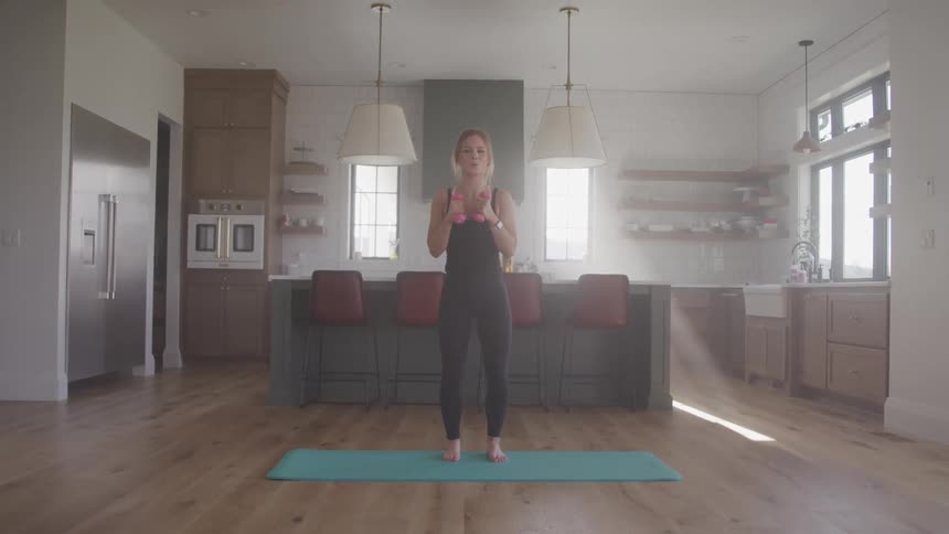 A woman stands on a yoga mat in her kitchen making boxing type jabs