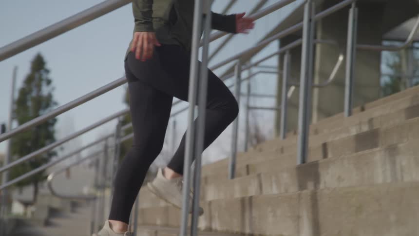 Woman with black tights a pair of grey running shoes runs up the stairs of a building