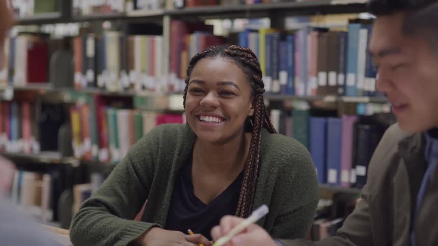 Three students laugh and talk in the library