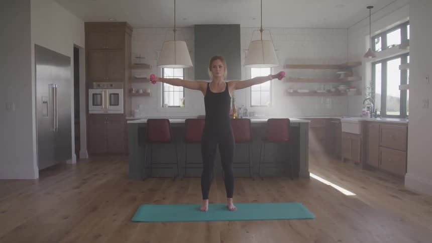 Young woman exercises lifting dumbbells over a mat on the kitchen at home