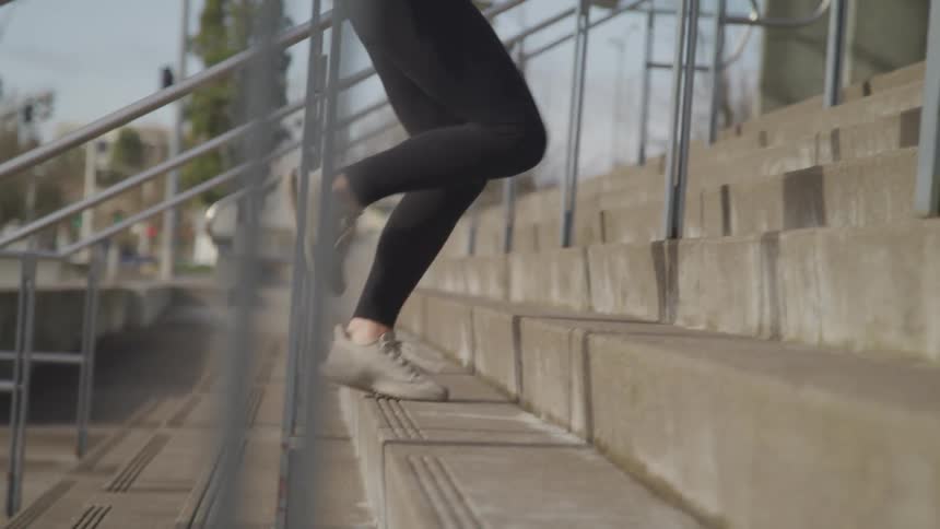 A woman is jogging up a flight of stairs outdoors in the morning