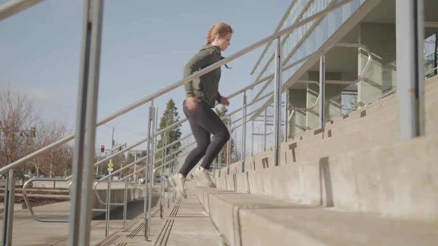 A woman in athletic wear runs up a set of cement stairs near an intersection on a sunny autumn day