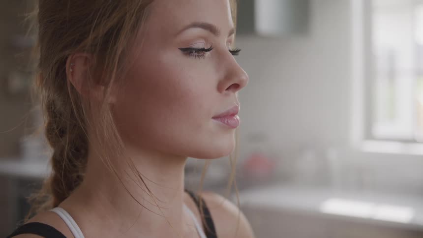 A lovely young woman looks up from her task while standing in a well lit kitchen