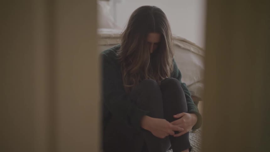 Stressed woman sitting on a rug leans against a bed in the bedroom