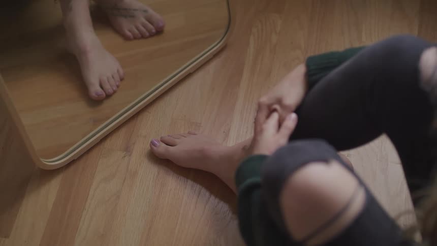 Woman with ripped jeans sits on the floor in front of a cheval glass