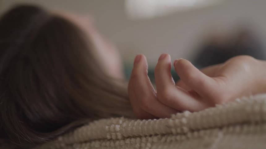 Woman with brown hair lies down on a bed and moves her fingers