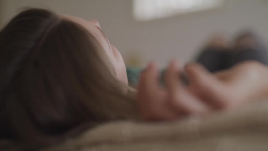 Woman lays on her back over a bed in a room at home