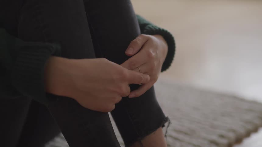 Woman sits on the floor with her knees up and her arms wrapped around her legs