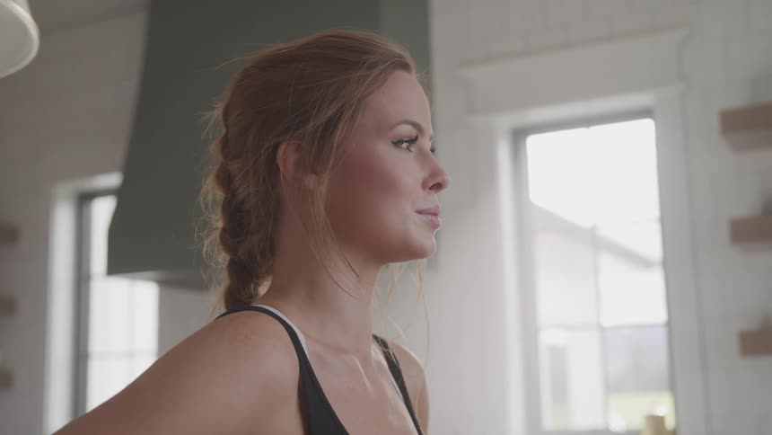 Blonde woman takes deep breath standing in kitchen looking straight ahead